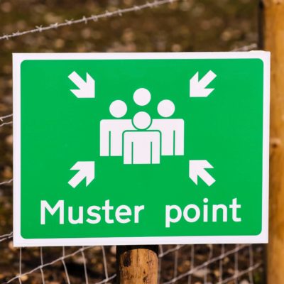 close-up of a green muster point sign in front of barbed wire