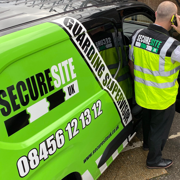a security guard on the phone stood next to a green and black branded secure site van